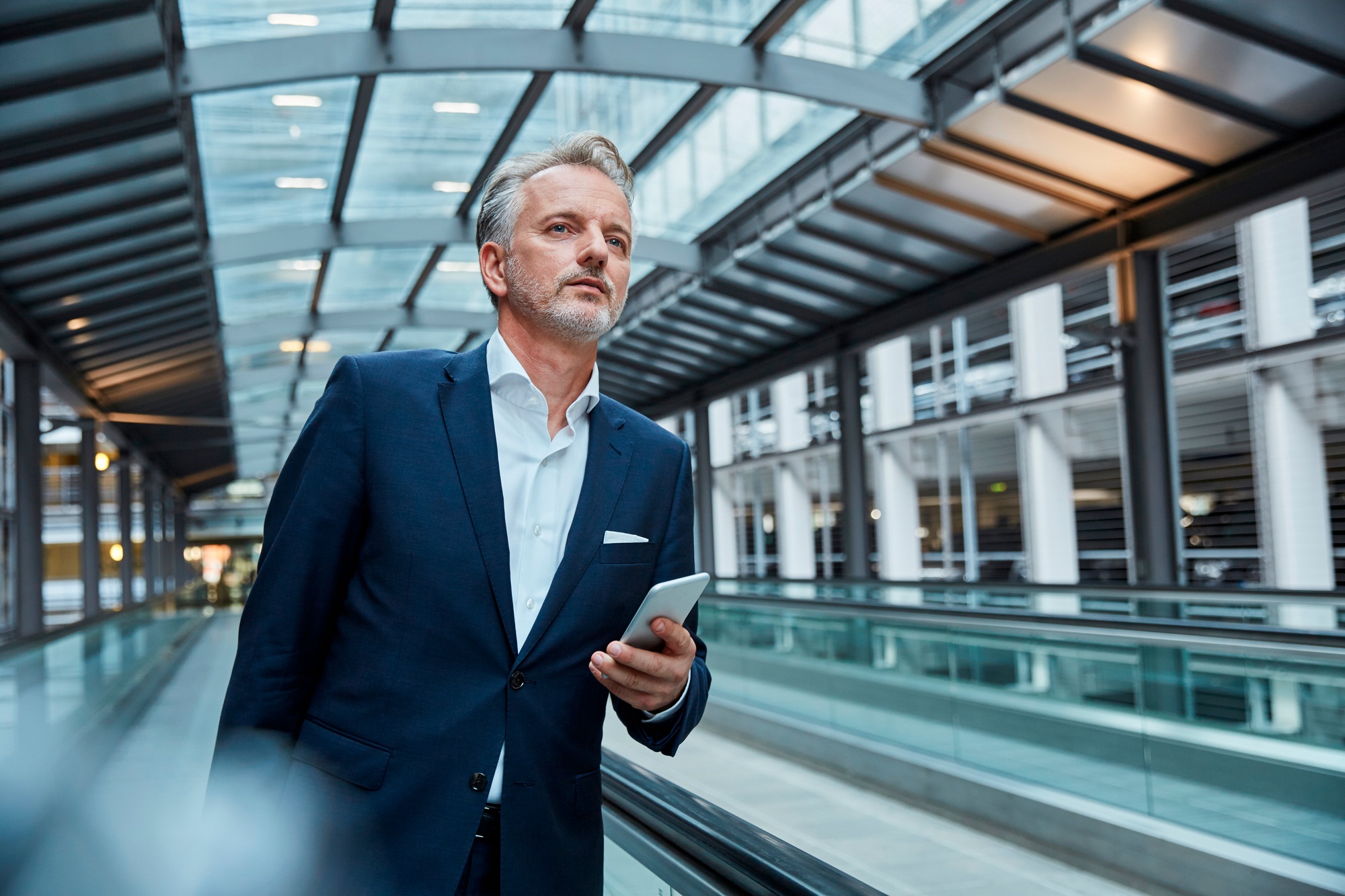 Businessman using smartphone at the airport, standing on moving walkway